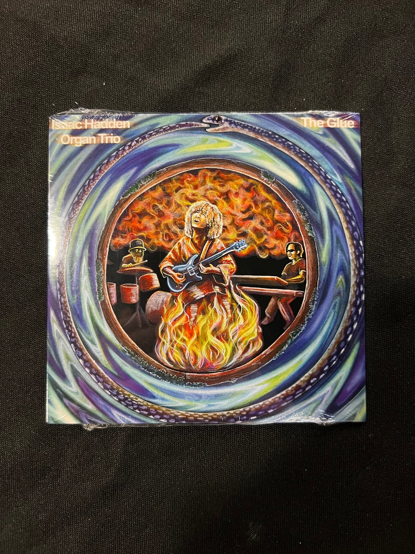 The Isaac Hadden Organ Trio CD art "The Glue" depicting Isaac Hadden on fire, surrounded by blue swirls of magic, resting on a black table cloth.