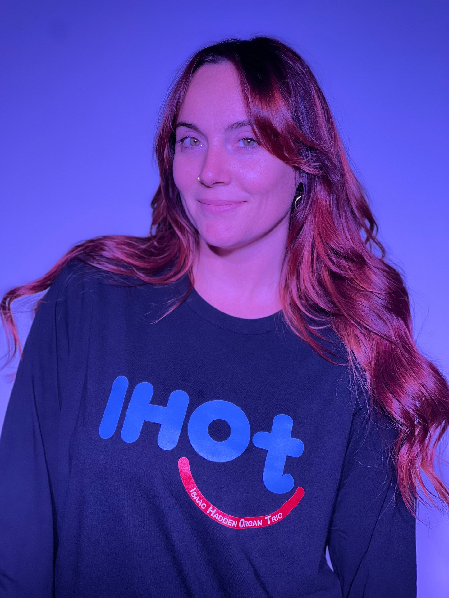 A young woman with brown hair and hazel eyes, smiling and wearing the Isaac Hadden Organ Trio black long sleeve T-shirt.