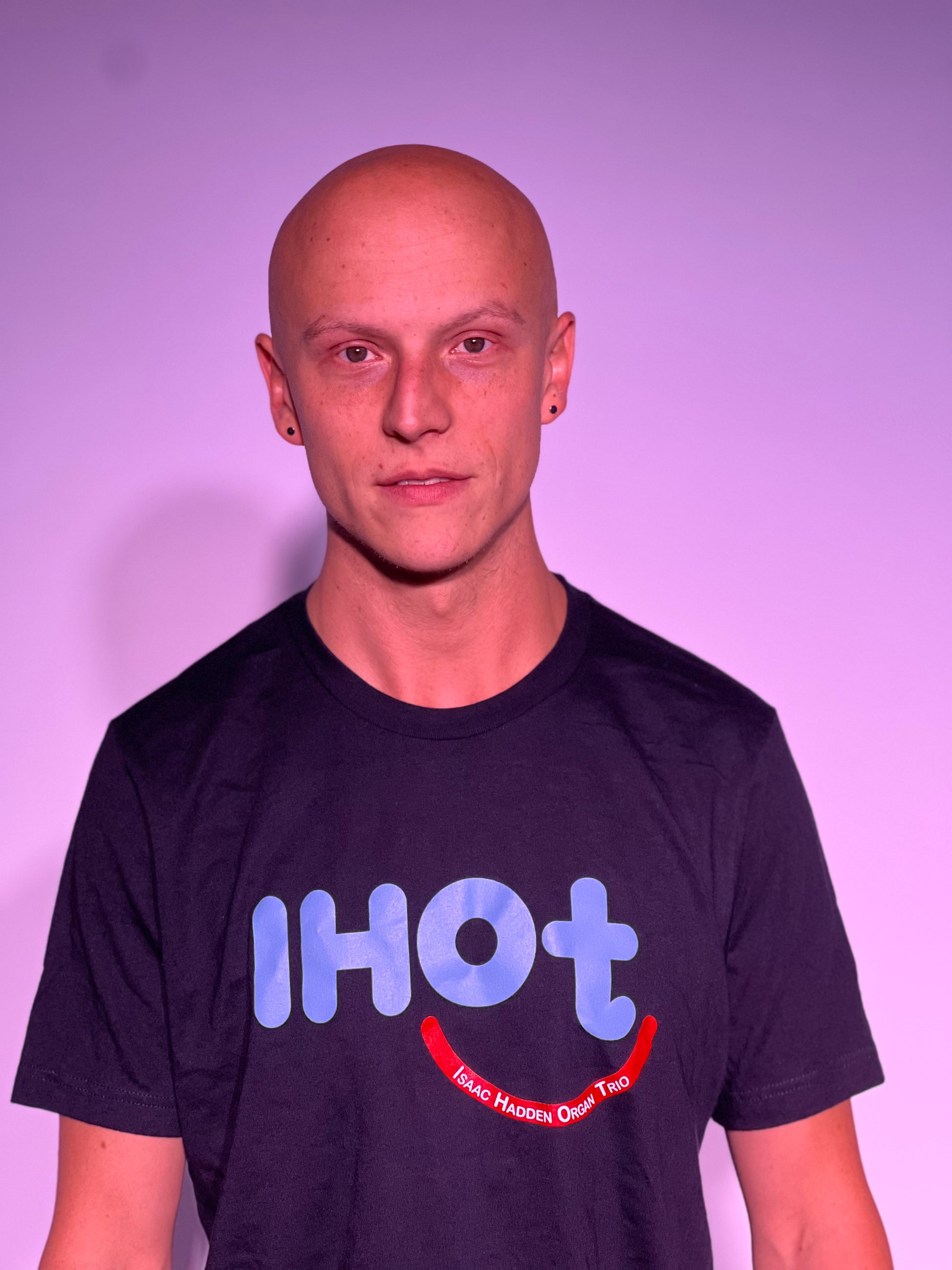 A young man with chiseled features, smiling and wearing the Isaac Hadden Organ Trio black T-shirt.