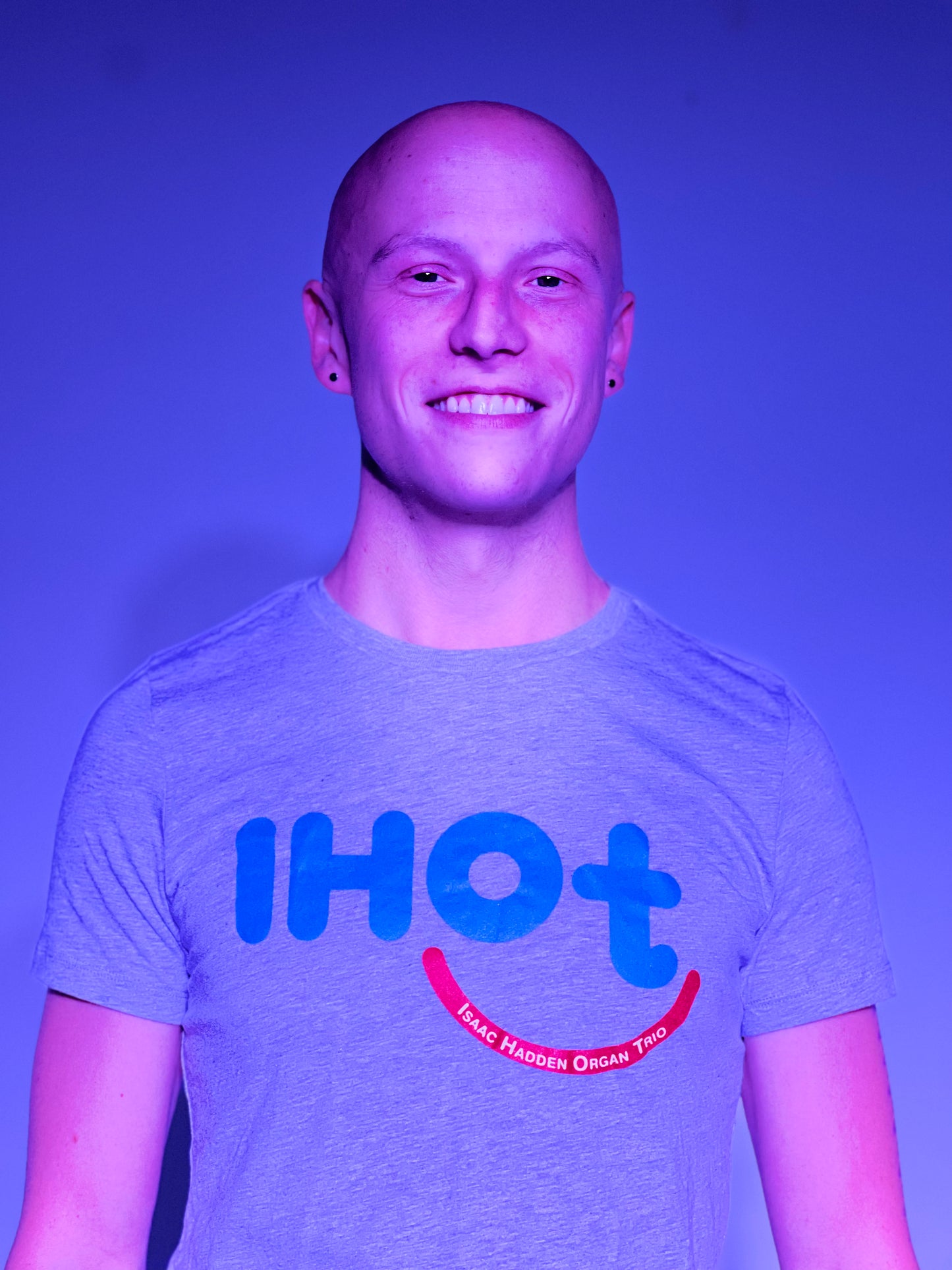 A young man with chiseled features, smiling and wearing the Isaac Hadden Organ Trio grey T-shirt.