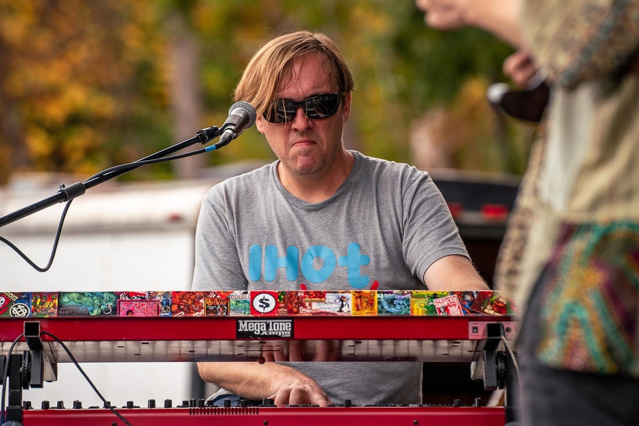 Bill Stevens playing the keys on a sunny day on an outdoor stage, wearing an Isaac Hadden Organ Trio grey T-shirt.